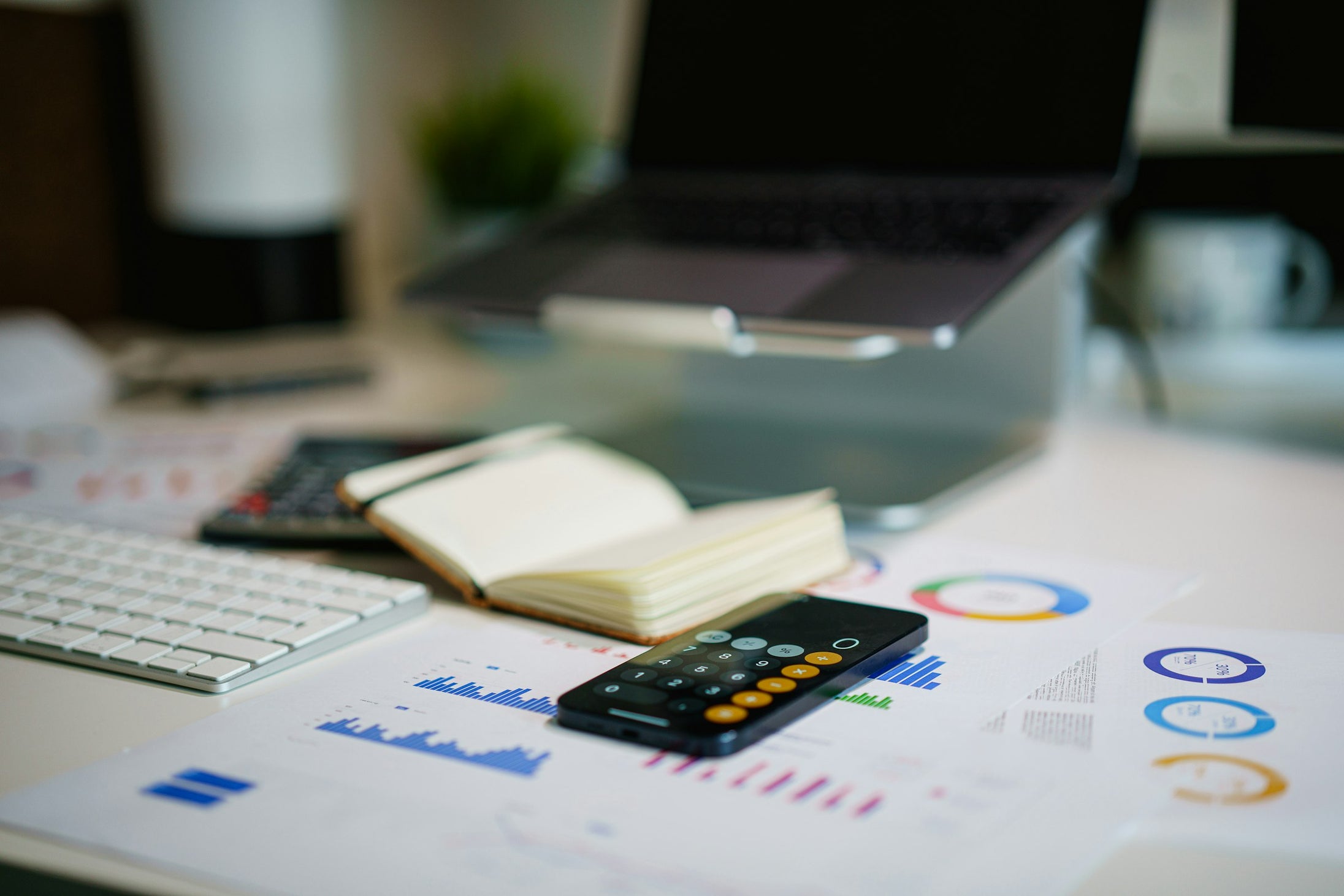 A desk with printed financial charts, a calculator and a smartphone, representing the cost and margin calculations behind a growing fashion brand